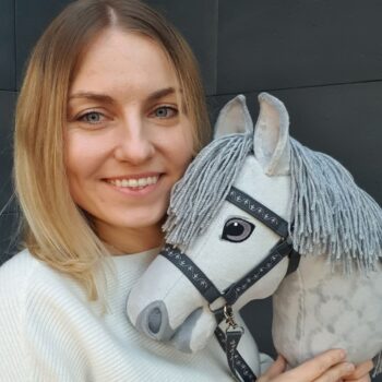 Gotowy Hobby Horse AS prezentowany przez autorkę instrukcji Toys by Kasia. Szary konik ma realistyczny kształt głowy, grzywę z włóczki i kantar.