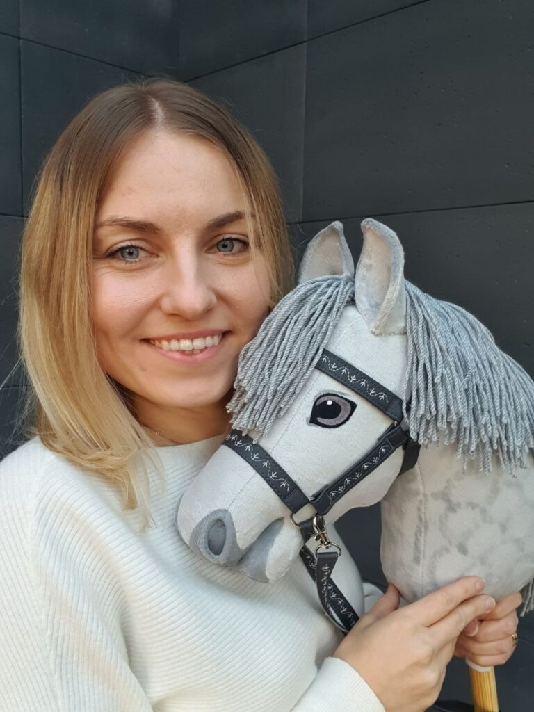 Gotowy Hobby Horse AS prezentowany przez autorkę instrukcji Toys by Kasia. Szary konik ma realistyczny kształt głowy, grzywę z włóczki i kantar.